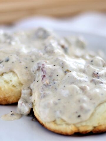 landscape view of sausage gravy over biscuits on white plate