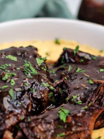 landscape view of pot roast and gravy atop a mound of grits in a white bowl.