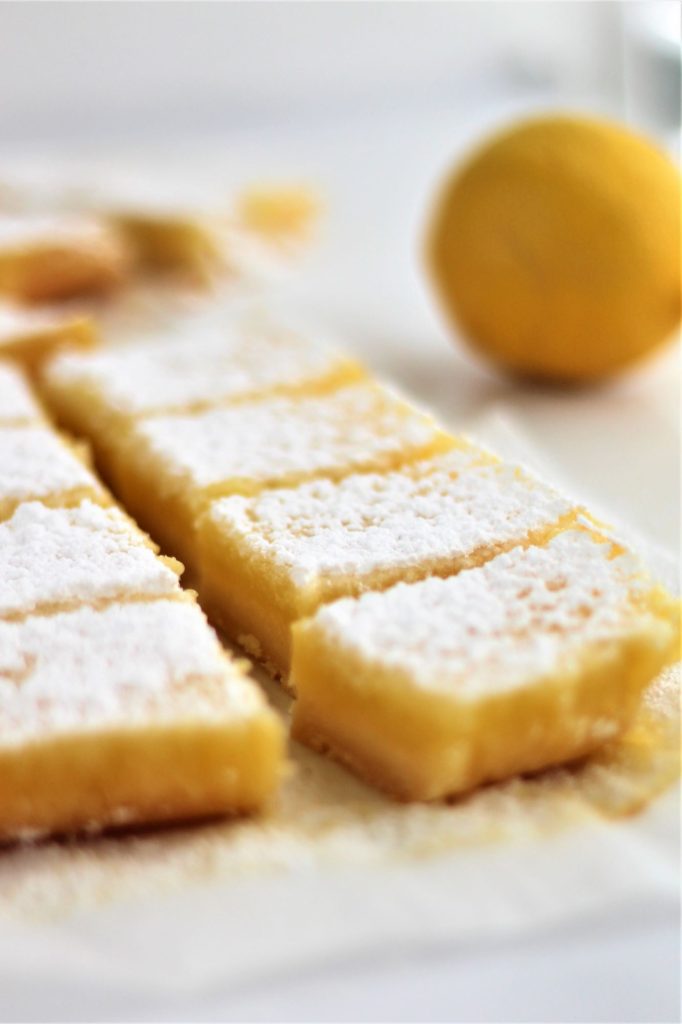 gf lemon bars in a row with a whole lemon in the background