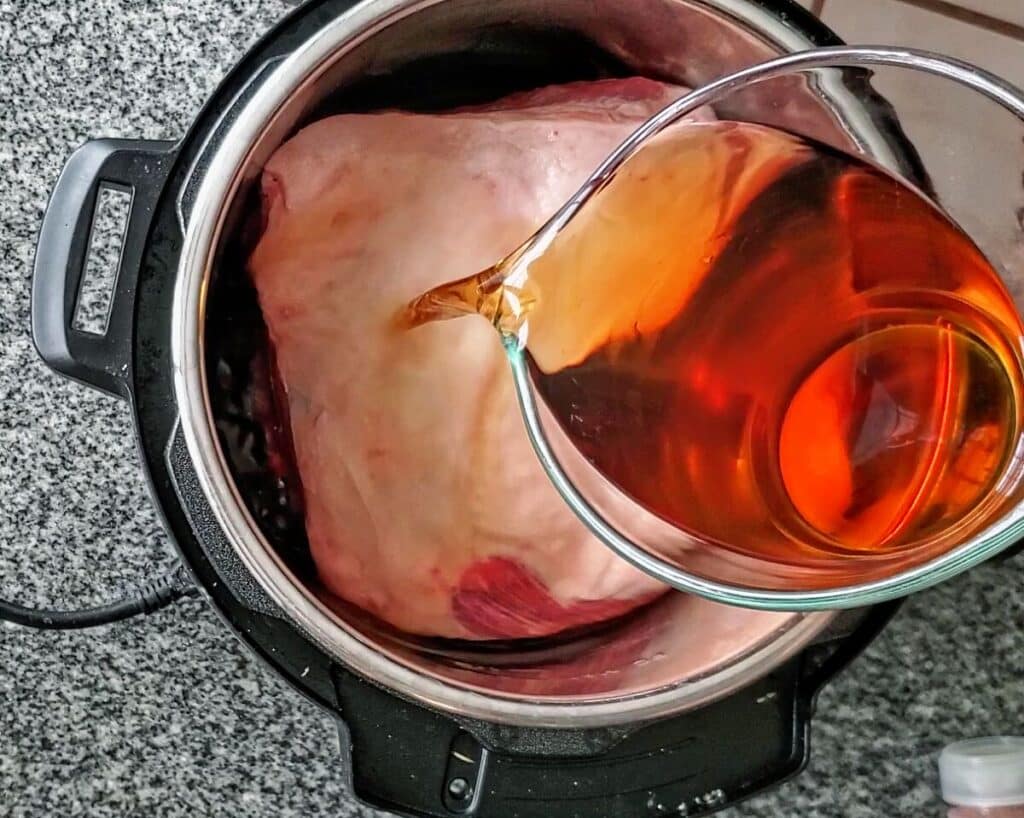 pouring apple cider and liquid smoke over pork shoulder in instant pot.