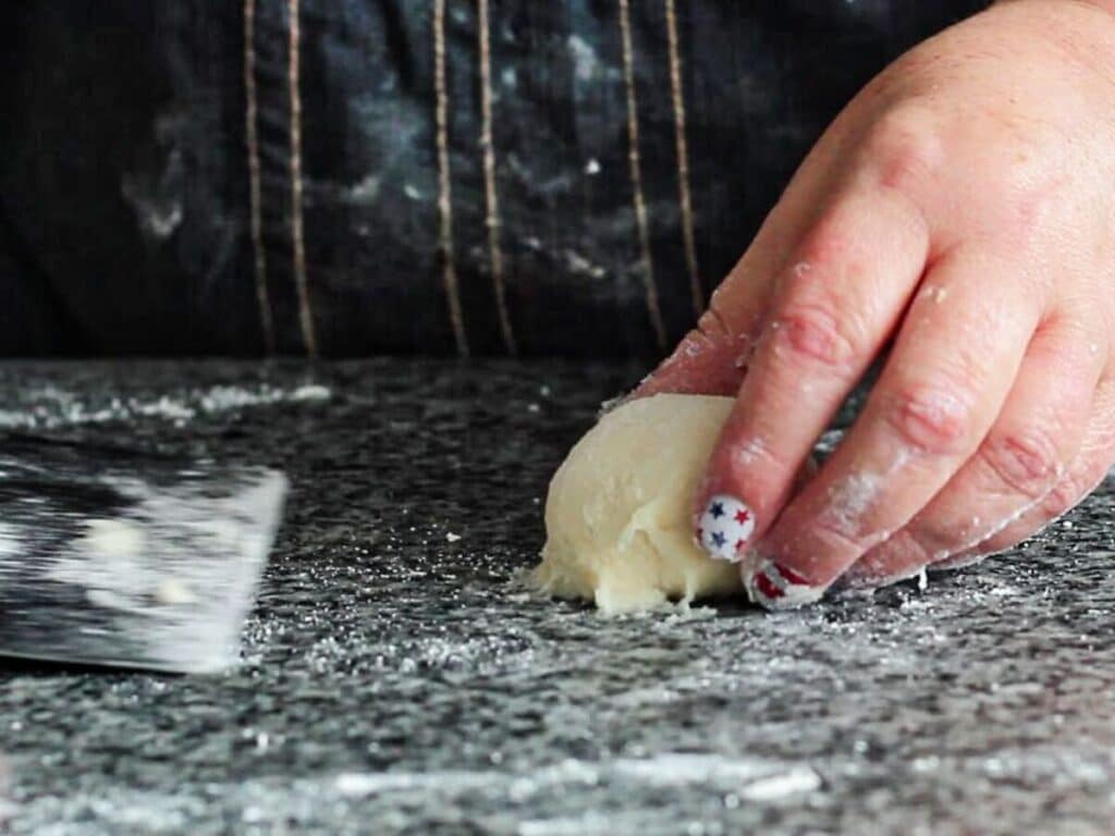 using bench scraper to scrape ball of dough from counter.