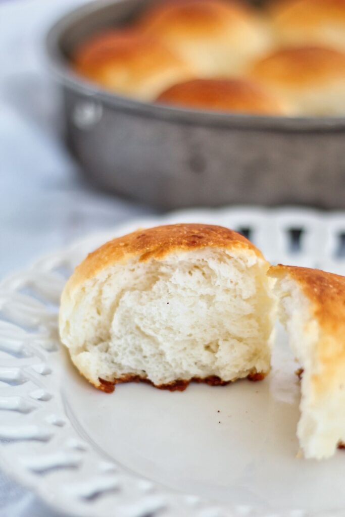 split open dinner roll on white plate with pan of rolls in background