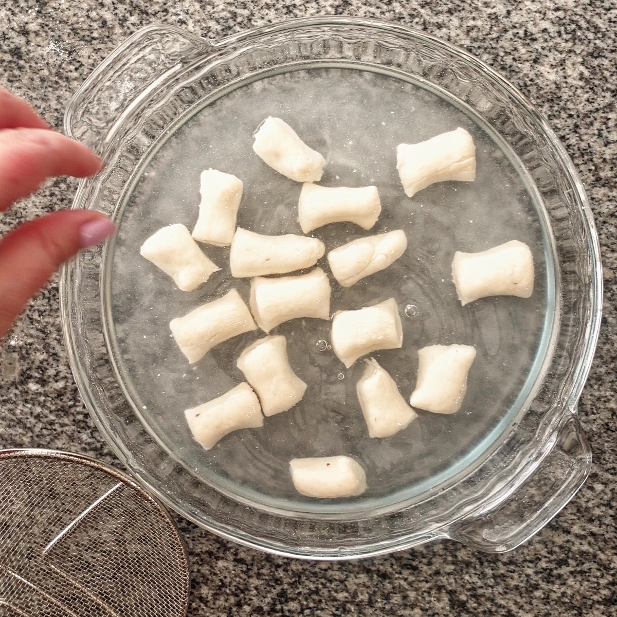 bathing pretzel bites in baking soda solution in glass pie plate.