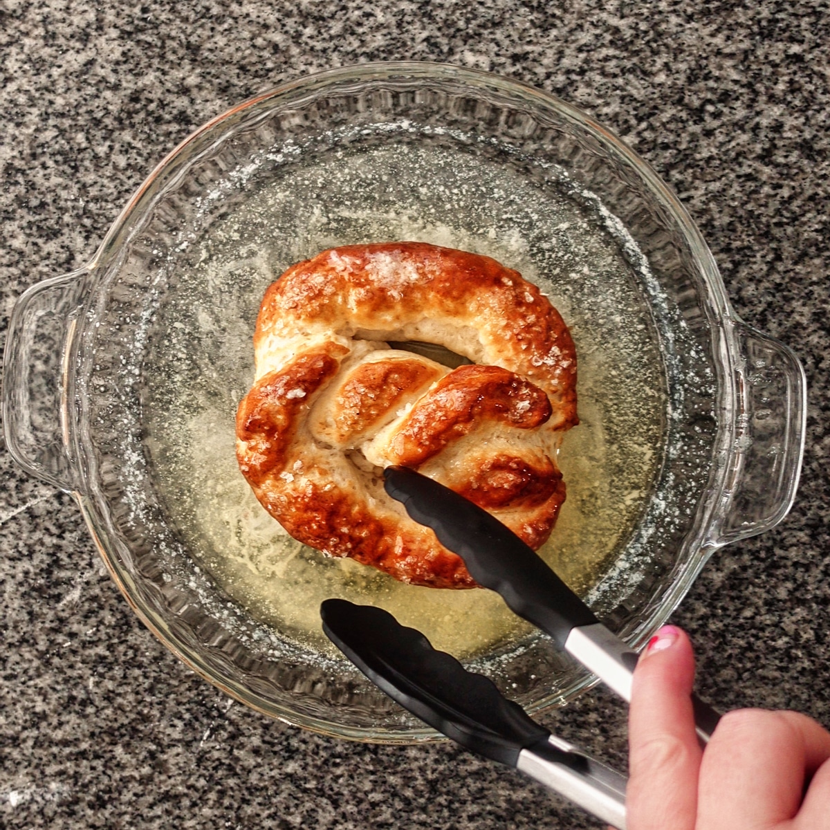 dipping pretzel in melted butter in glass pie plate.