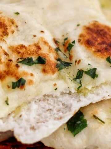 landscape view of torn apart naan atop a stack of whole naan.