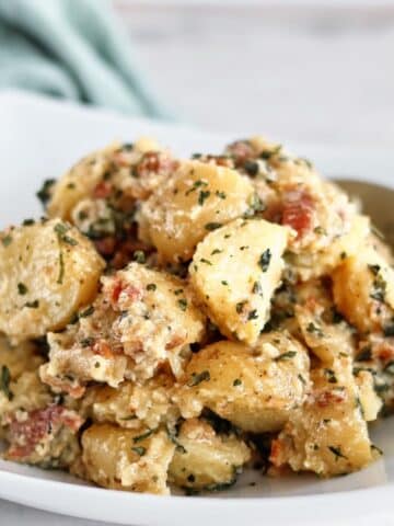 basil potato salad in white square bowl with green towel in the background.