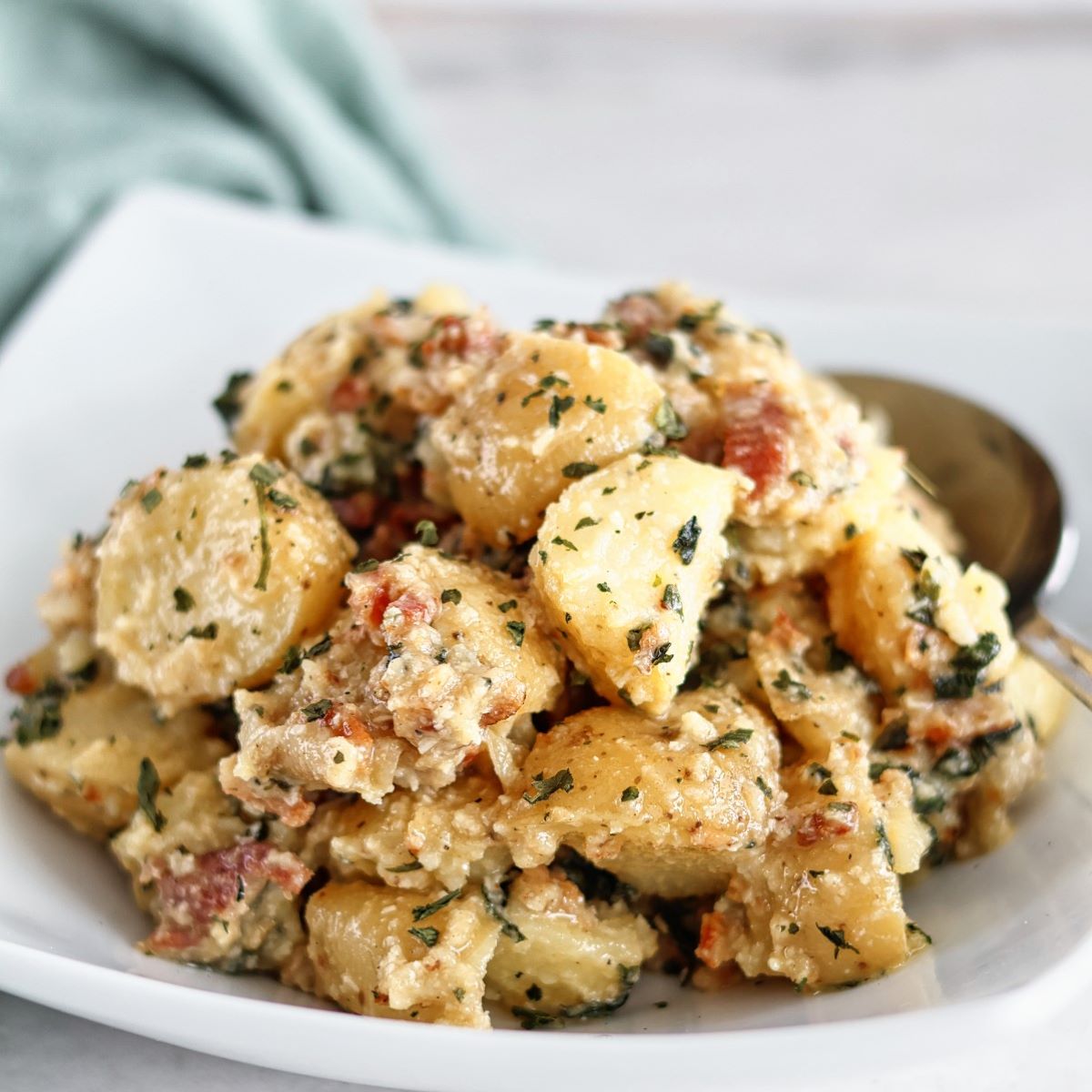 basil potato salad in white square bowl with green towel in the background.