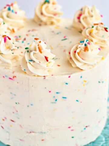 landscape view of whole slice of gf funfetti cake on blue cake stand over white flour sac towel