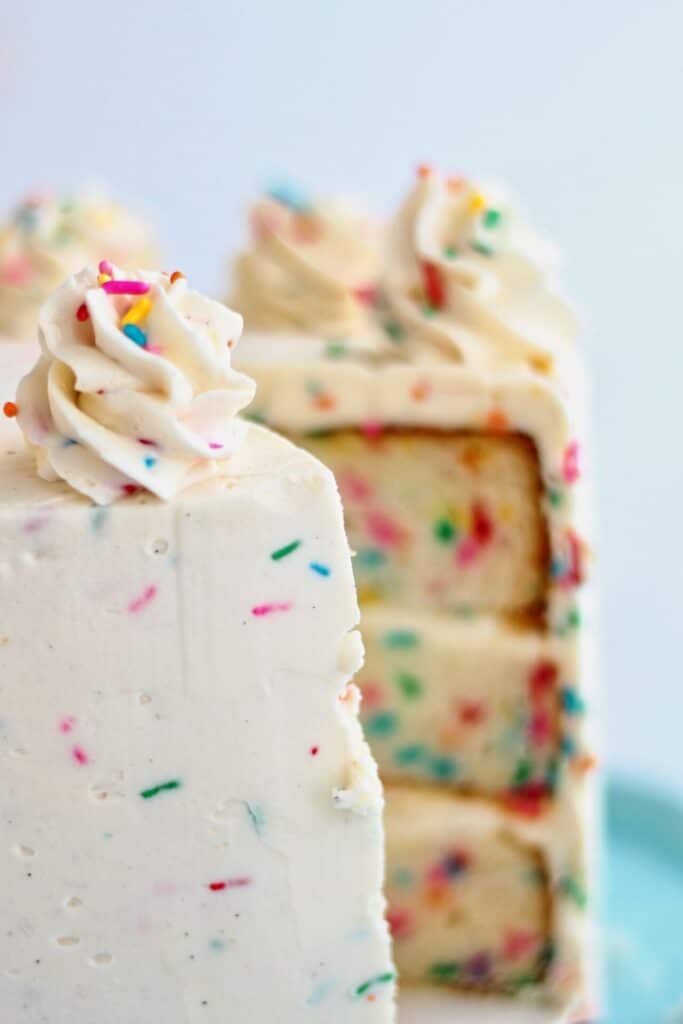 whole funfetti cake on blue cake stand with one slice removed from it