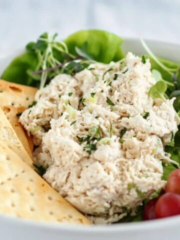 landscape view of classic chicken salad on a bed of lettuce in a white bowl with red grapes and crackers alongside.