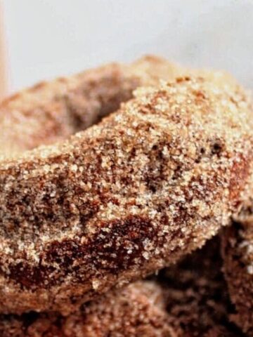 landscape view of gf apple cider donuts stacked on plate with apple cider in the background.