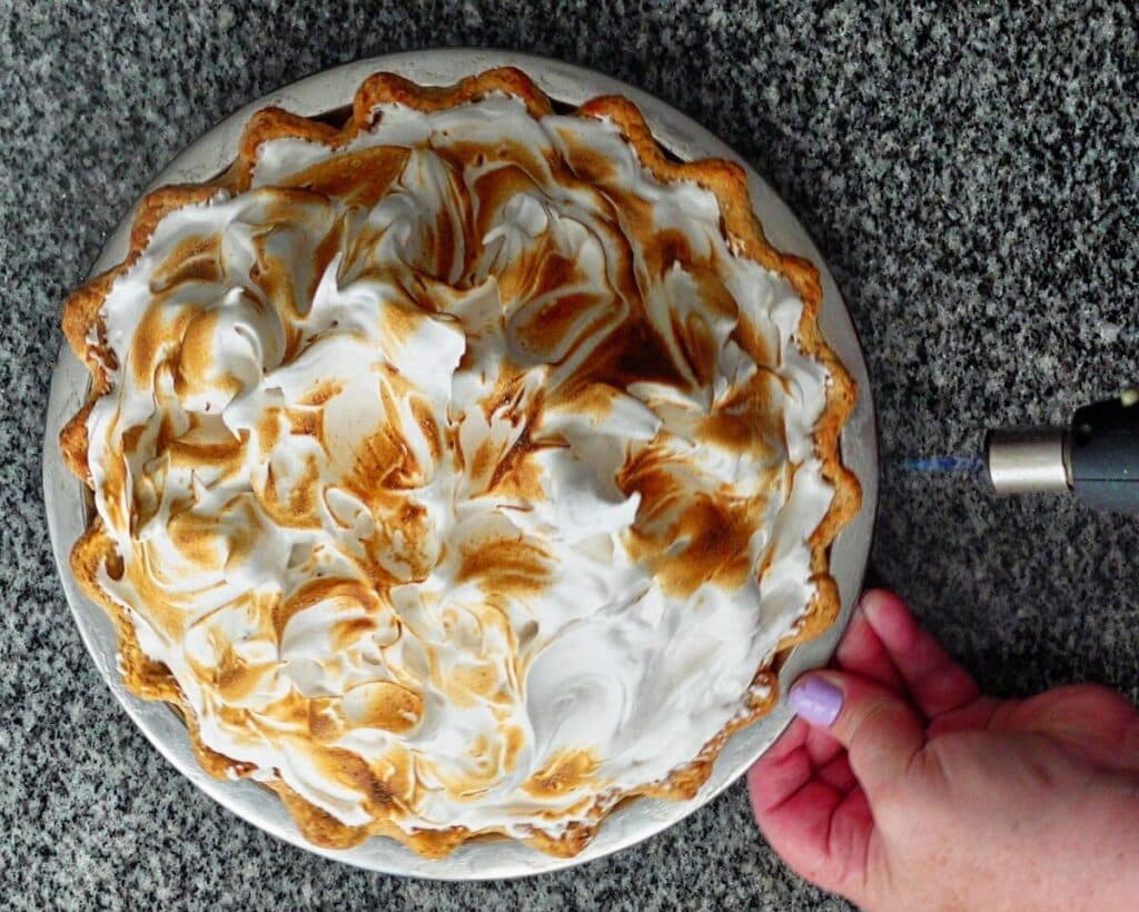 toasting meringue on top of pie with kitchen torch.
