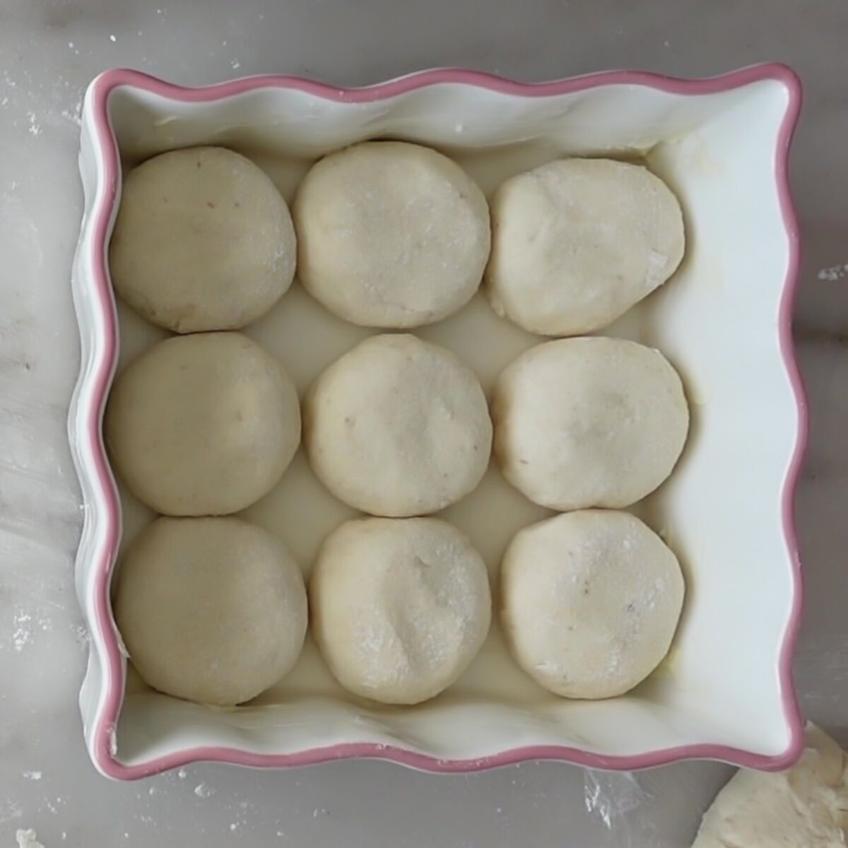 shaped hawaiian rolls in white square baking dish with pink trim.