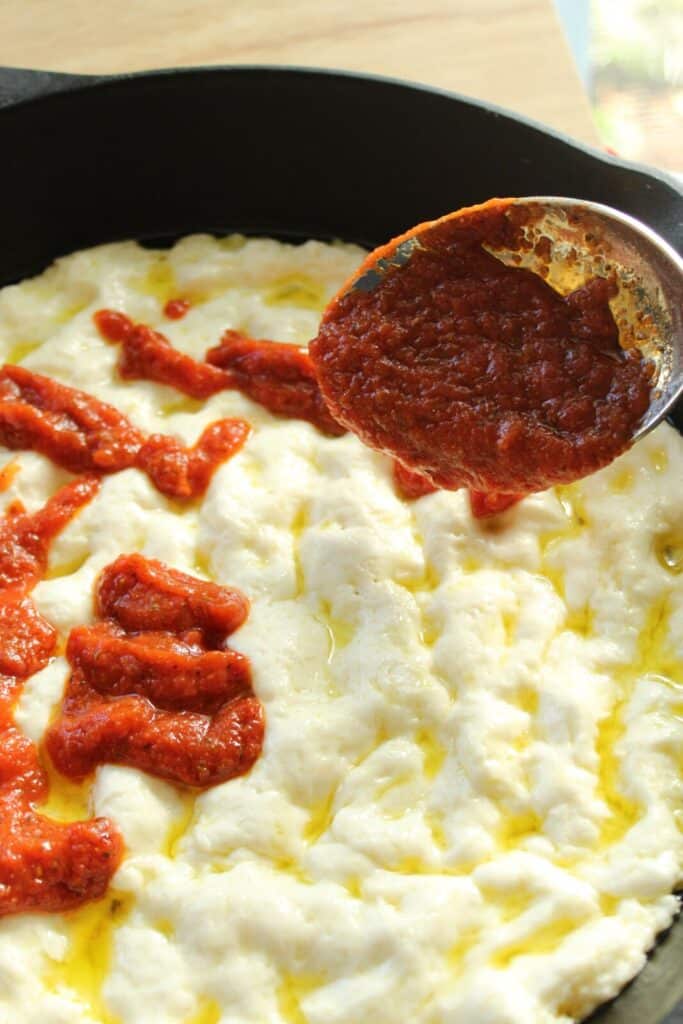 adding pizza sauce to risen gluten free pan pizza dough in cast iron skillet.