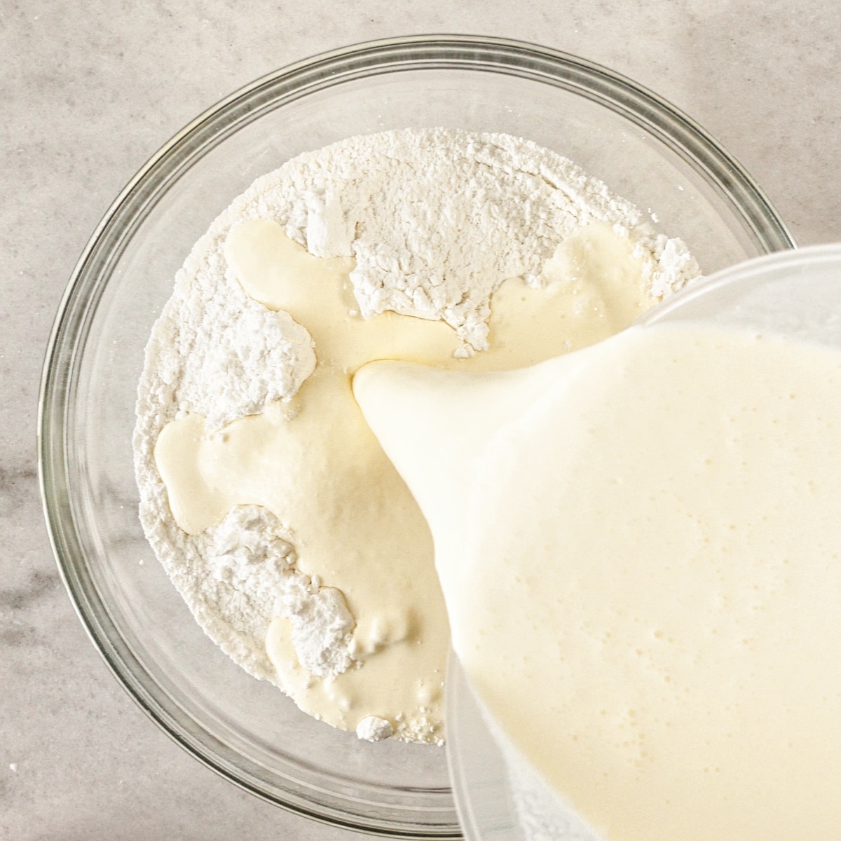 pouring wet ingredients into the middle of dry ingredients in large glass bowl.