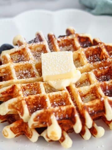 two waffles on large white scalloped plate with berries alongside.