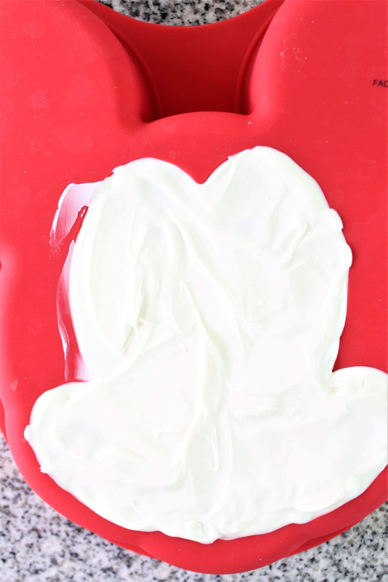 white chocolate spread onto mickey face of red silicone cake mold.