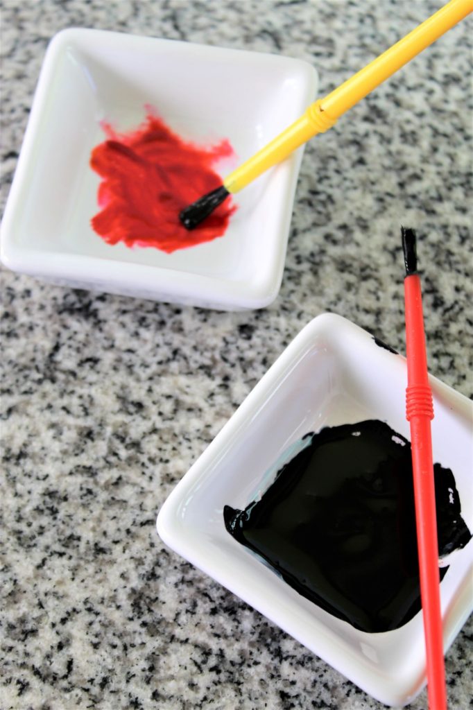 black and red gel food colors in small white square bowls
