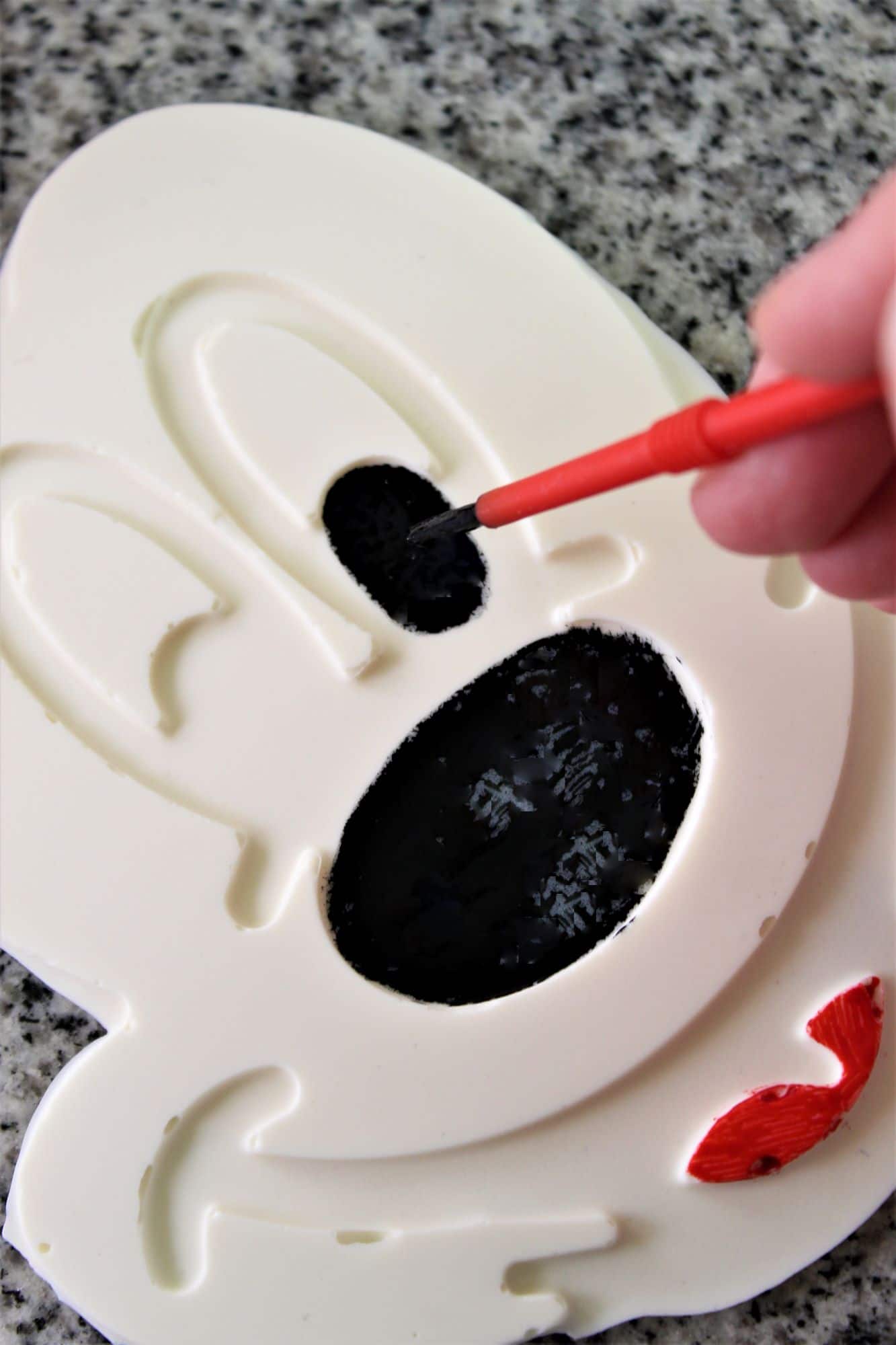 painting red and black gel food colors on the white chocolate mickey face.