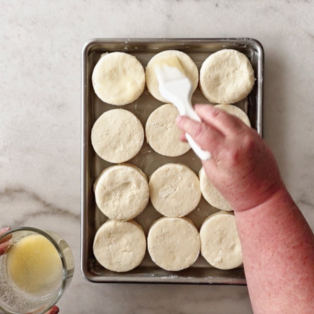 brushing unbaked biscuits with melted butter on baking sheet.