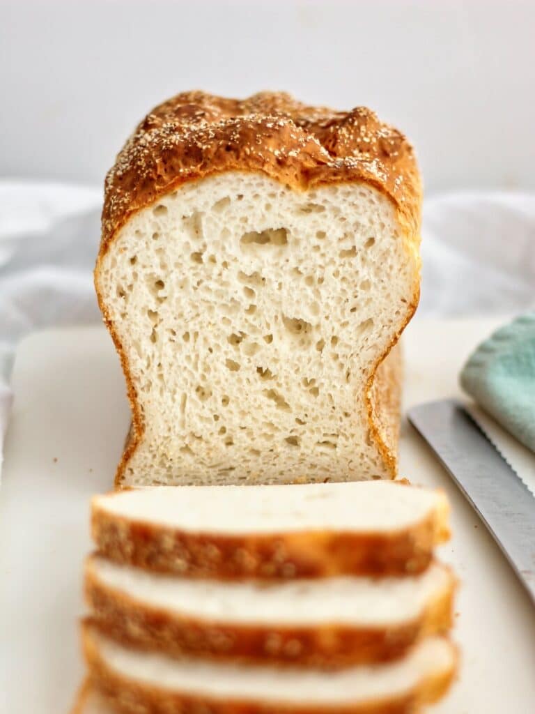 front view of half sliced loaf of English muffin bread on white plastic cutting board.