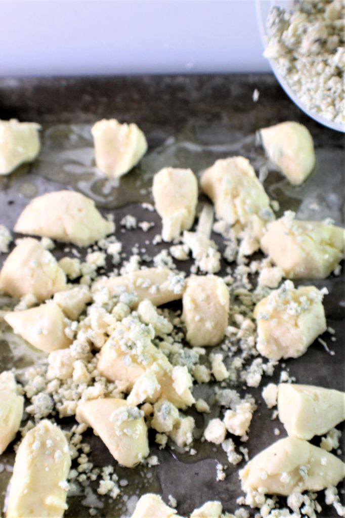 sprinkling blue cheese over biscuits on baking sheet