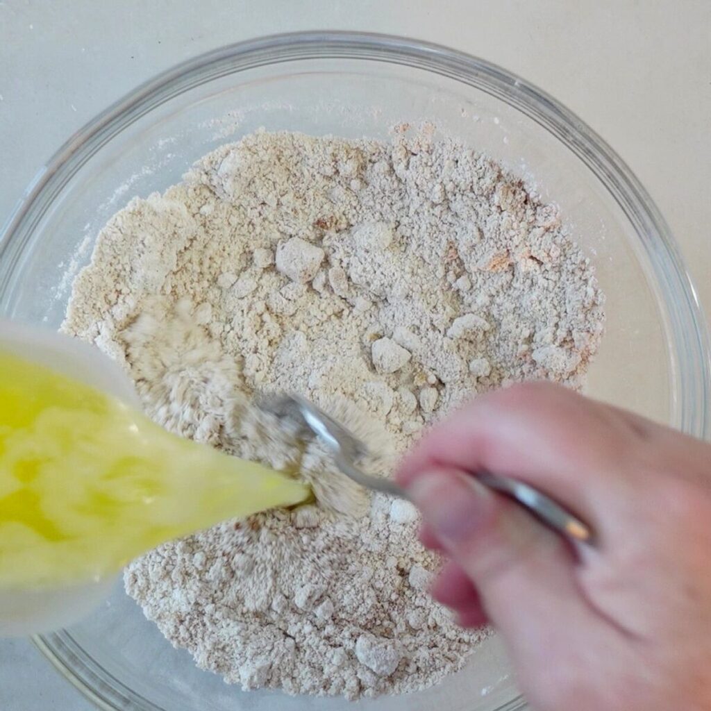 pouring melted butter into crumble ingredients in bowl.