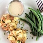 two crab cakes on a white plate with sauce and green beans