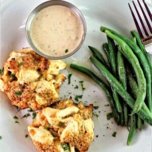 two gluten free crab cakes on white plate with remoulade sauce and green beans.