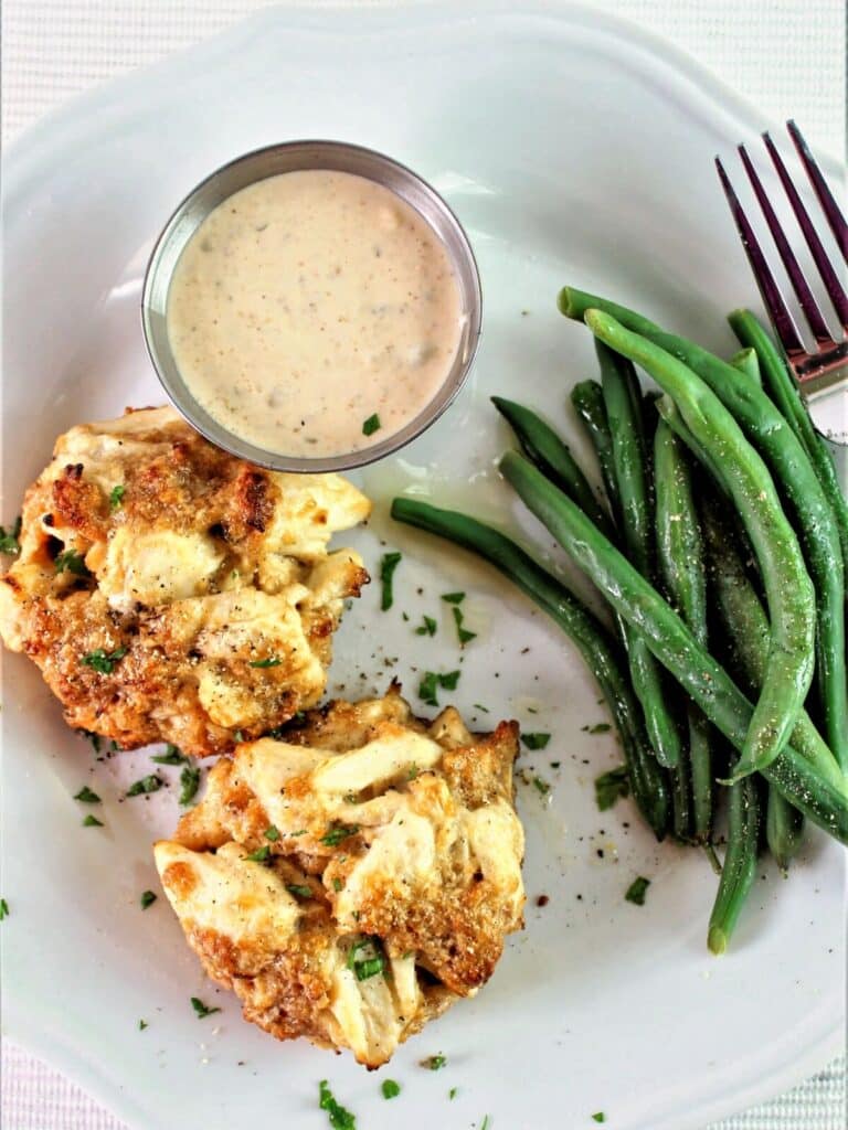 two gluten free crab cakes on white plate with remoulade sauce and green beans.