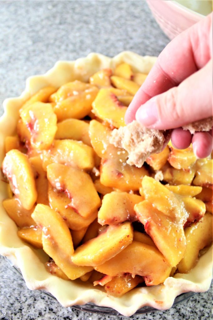 sprinkling crumb mixture over peaches in pie