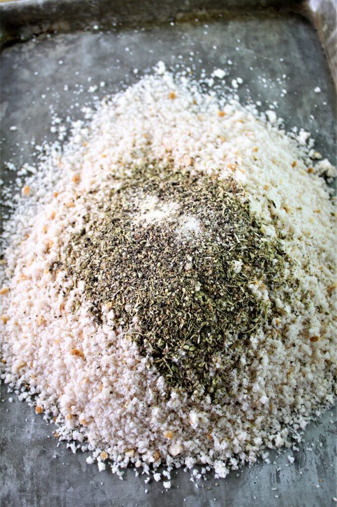 breadcrumbs in a pile on baking sheet with dried herbs on top