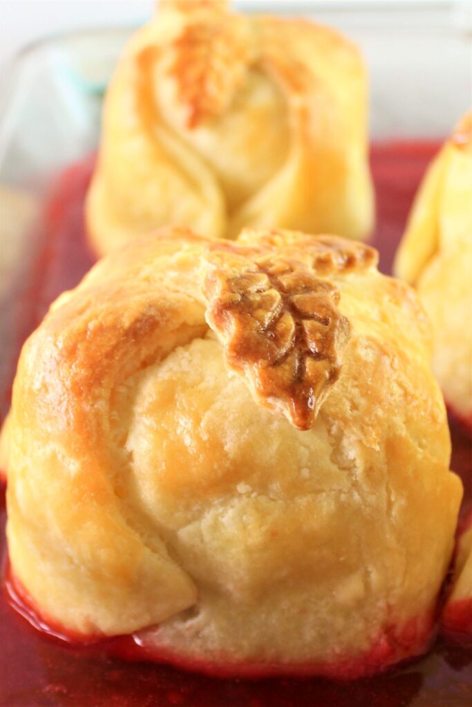 apple dumplings in glass baking dish sitting in a bright red sauce