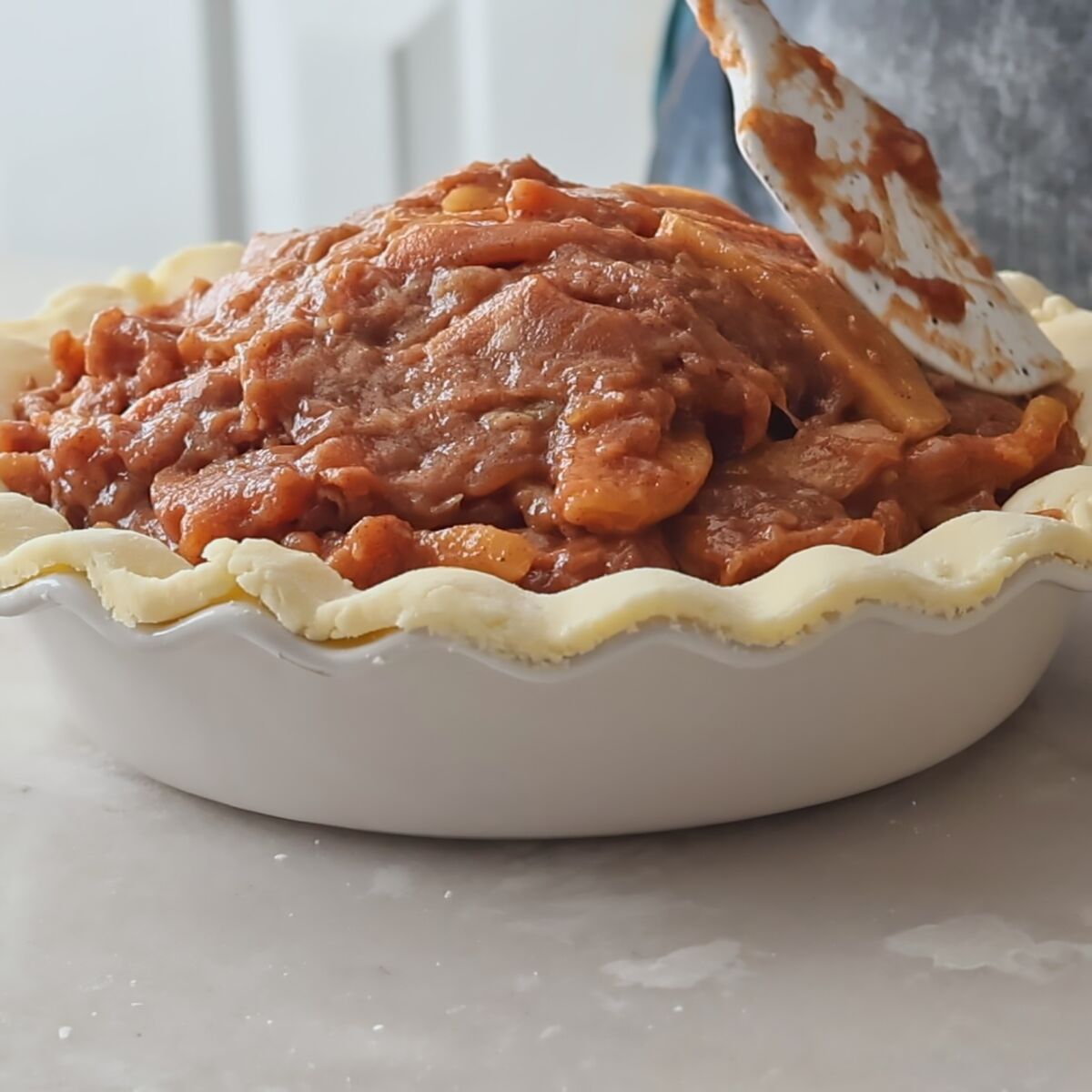 adding apple pie filling to bottom pie crust.