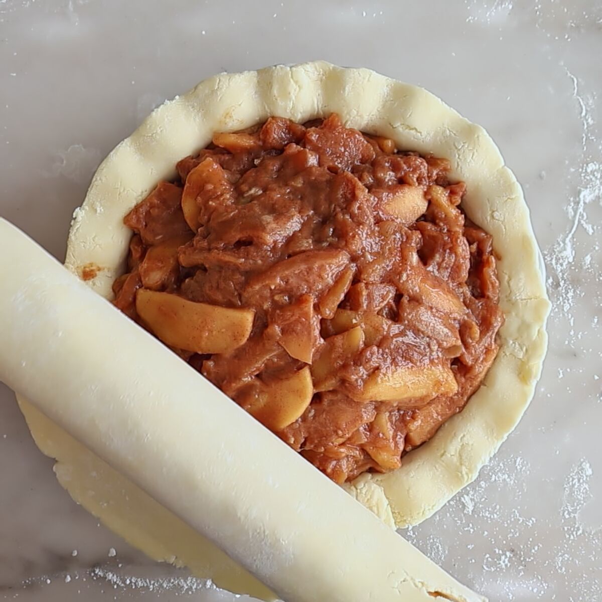 unrolling top crust over apple pie filling.