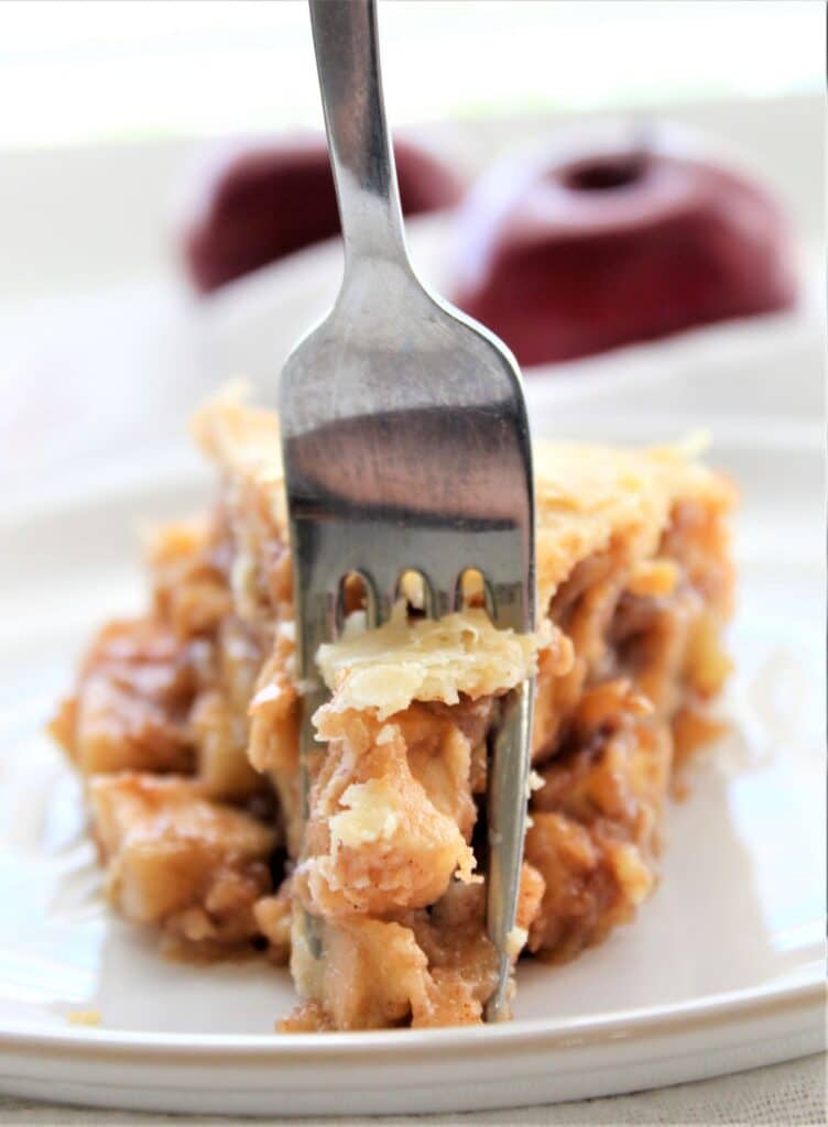 fork cutting through slice of apple pie on white plate