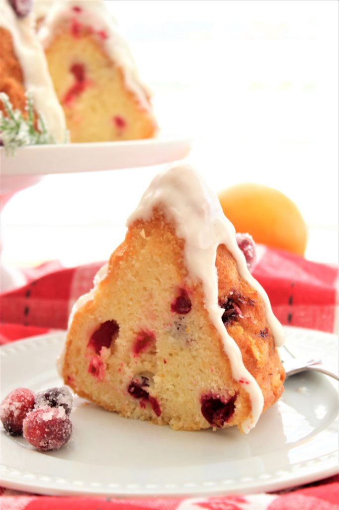 slice of gluten free cranberry orange bundt cake on white plate over red checked napkin