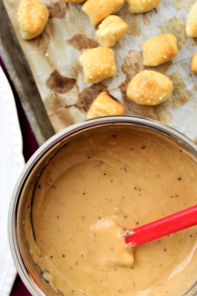 beer cheese dip in saucepan with soft pretzel bites in the background