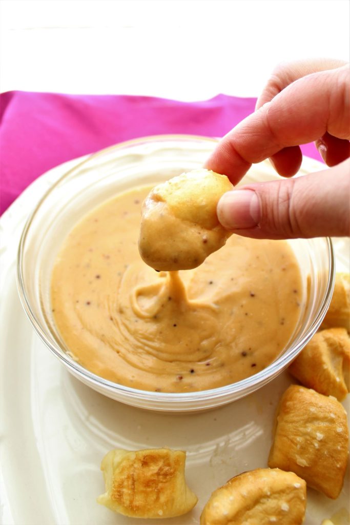 dipping pretzel bite into cheese dip