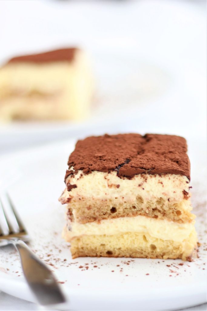 slice of tiramisu on white plate with silver fork