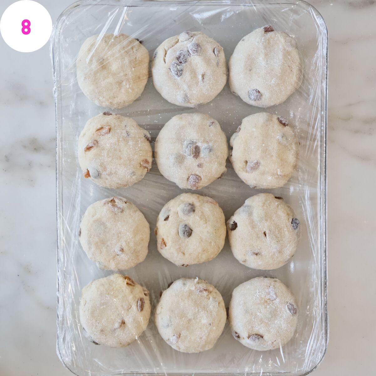 unbaked rolls in rectangular glass baking dish covered with plastic wrap.