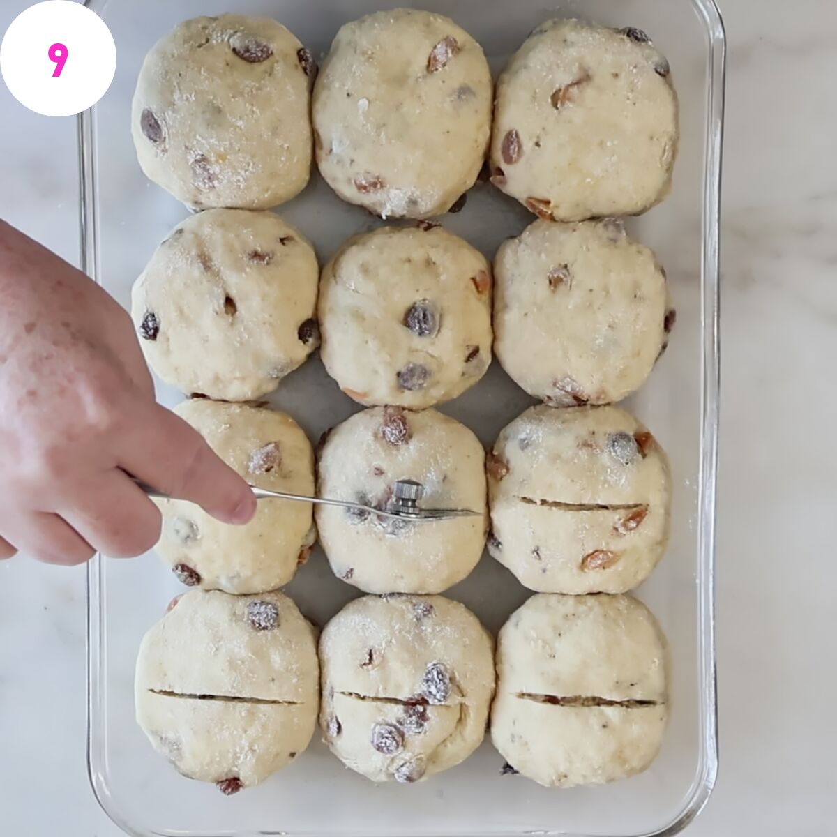 cutting cross into prebaked buns in glass rectangular baking dish.