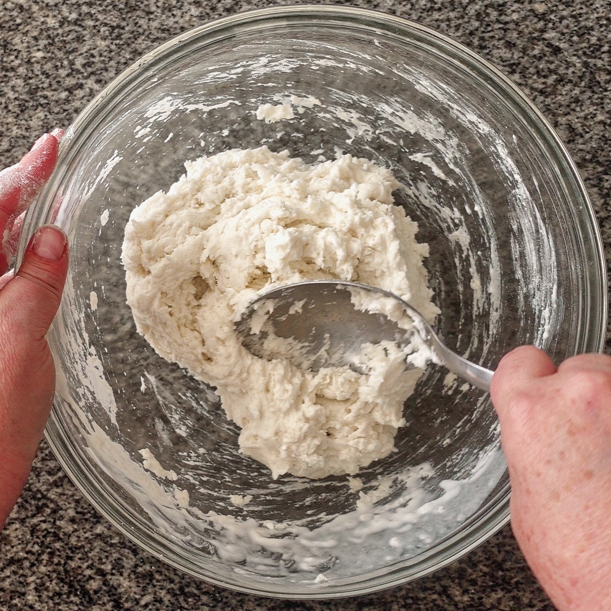 bringing dough together with spoon in large glass bowl.