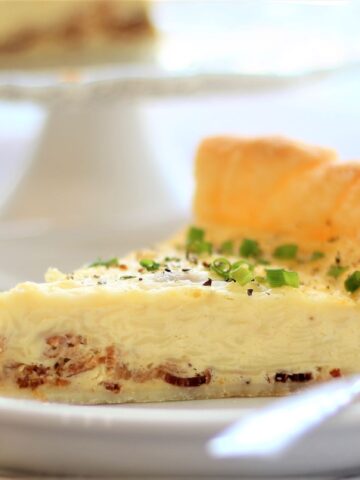 slice of quiche on white plate with rest of quiche on cake stand