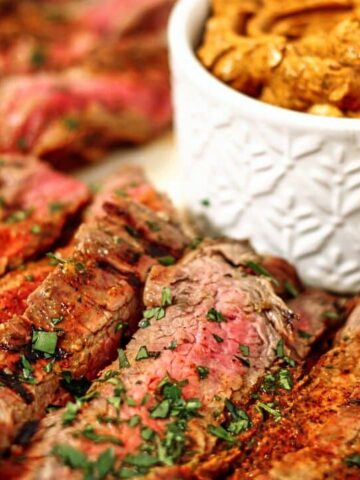 landscape view of sliced flank steak on white platter with chili butter in small white ramekin.