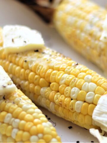 grilled corn on the cob with large pats of butter on white platter