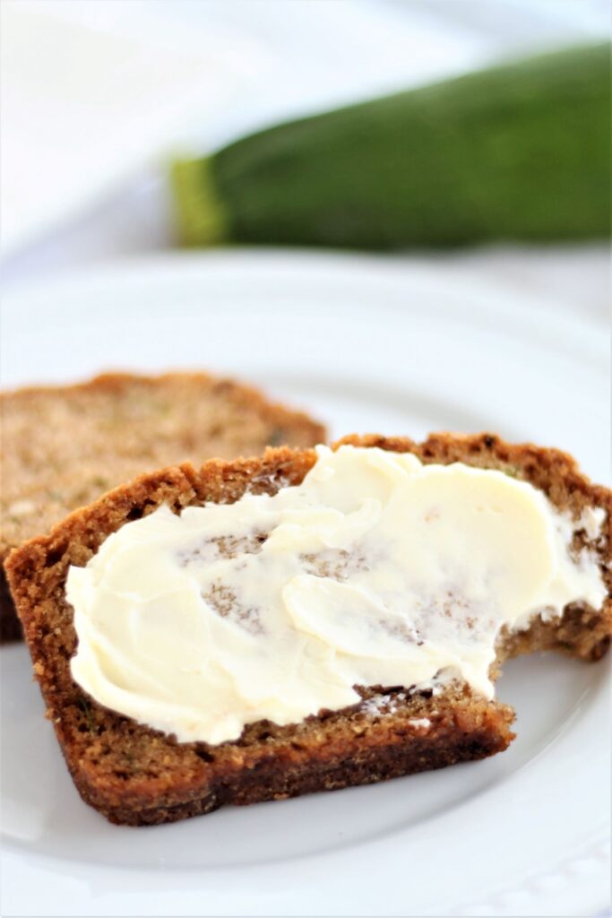 two slices of zucchini bread on white plate, one spread with butter and bit into