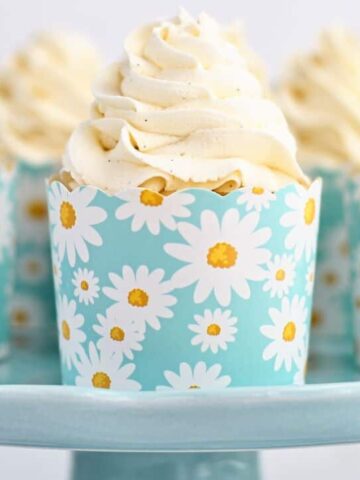 several perfect gluten free vanilla cupcakes in daisy printed cardboard cupcake liners on robin's egg blue cake stand.