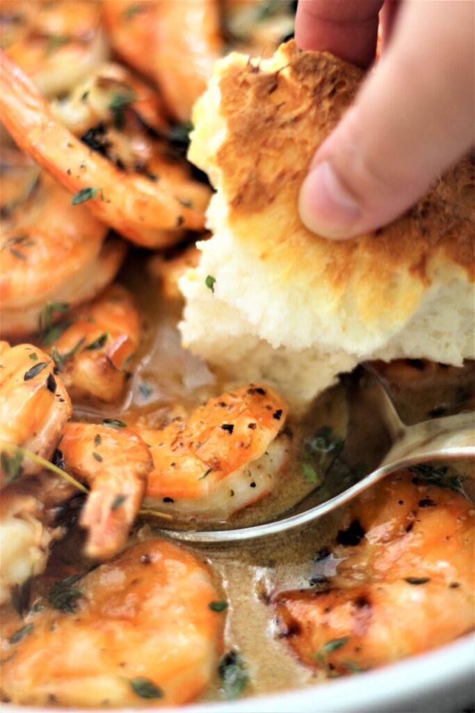 shrimp in a white bowl and dipping the bread into the sauce