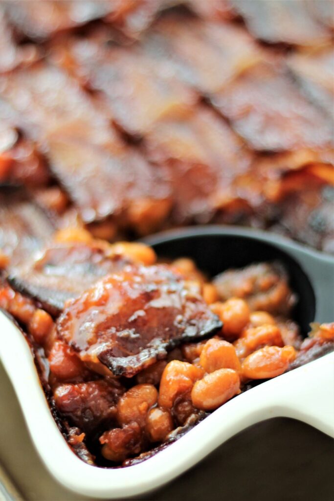 scooping baked beans with black spoon from white casserole dish